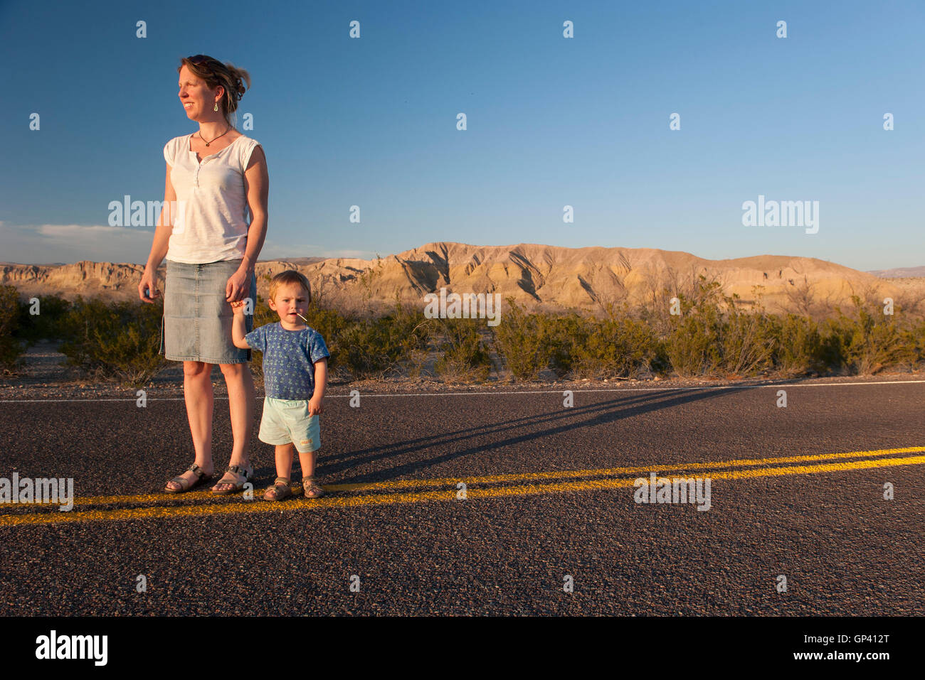 Mutter und Kleinkind Sohn gehen gemeinsam auf asphaltierten Straße durch Wüste Stockfoto