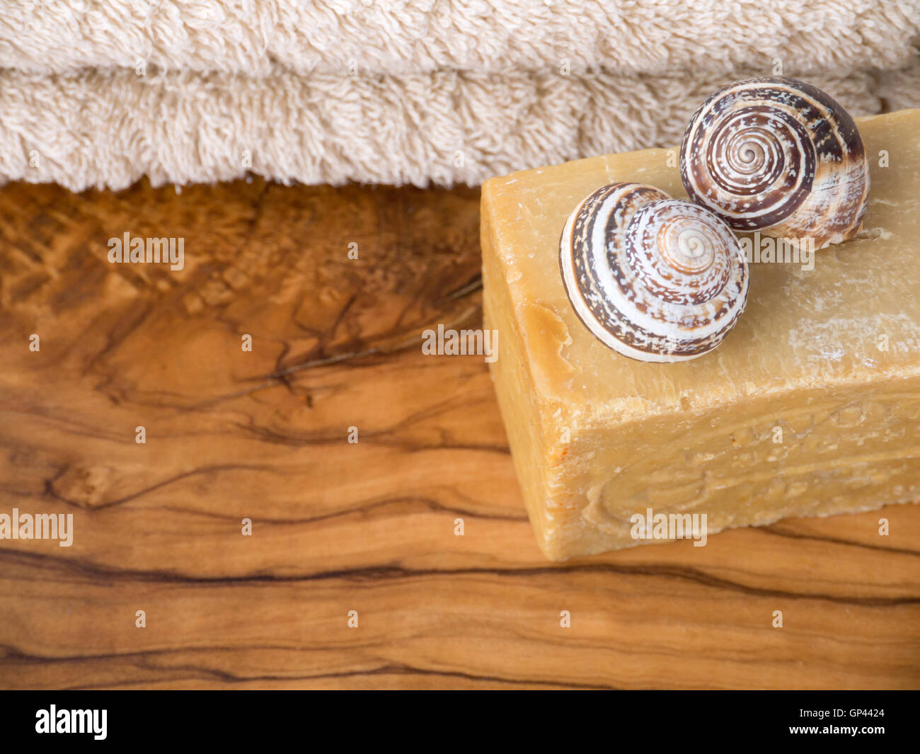 Selbstgemachte Seife, zwei Schneckenhäuser und Terry Handtuch auf den Olivenbaum texturiert Holzbrett Stockfoto