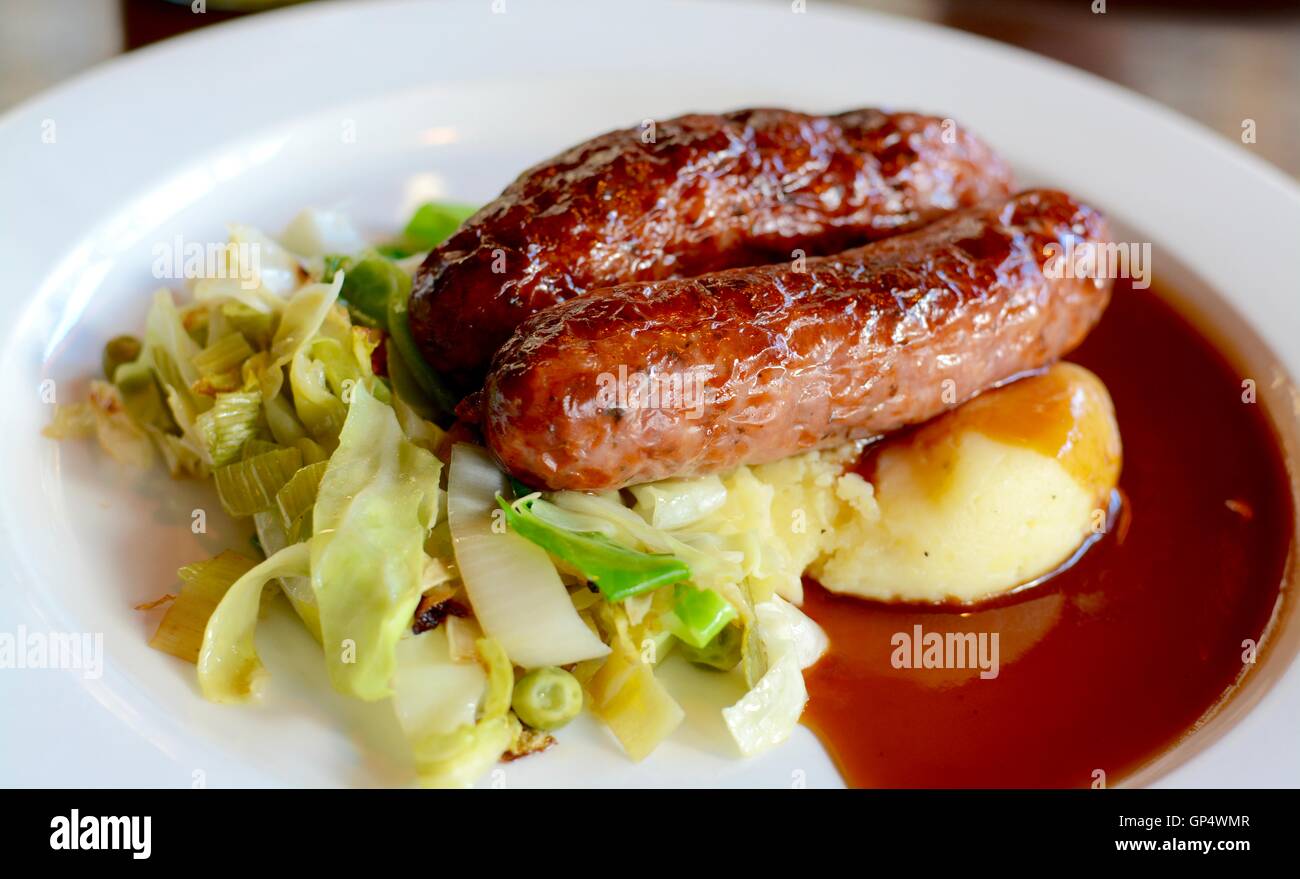 Würstchen und Kartoffelbrei mit saisonalen Gruenen mit Rotwein Soße auf einem weißen Teller serviert - Filter angewendet Stockfoto