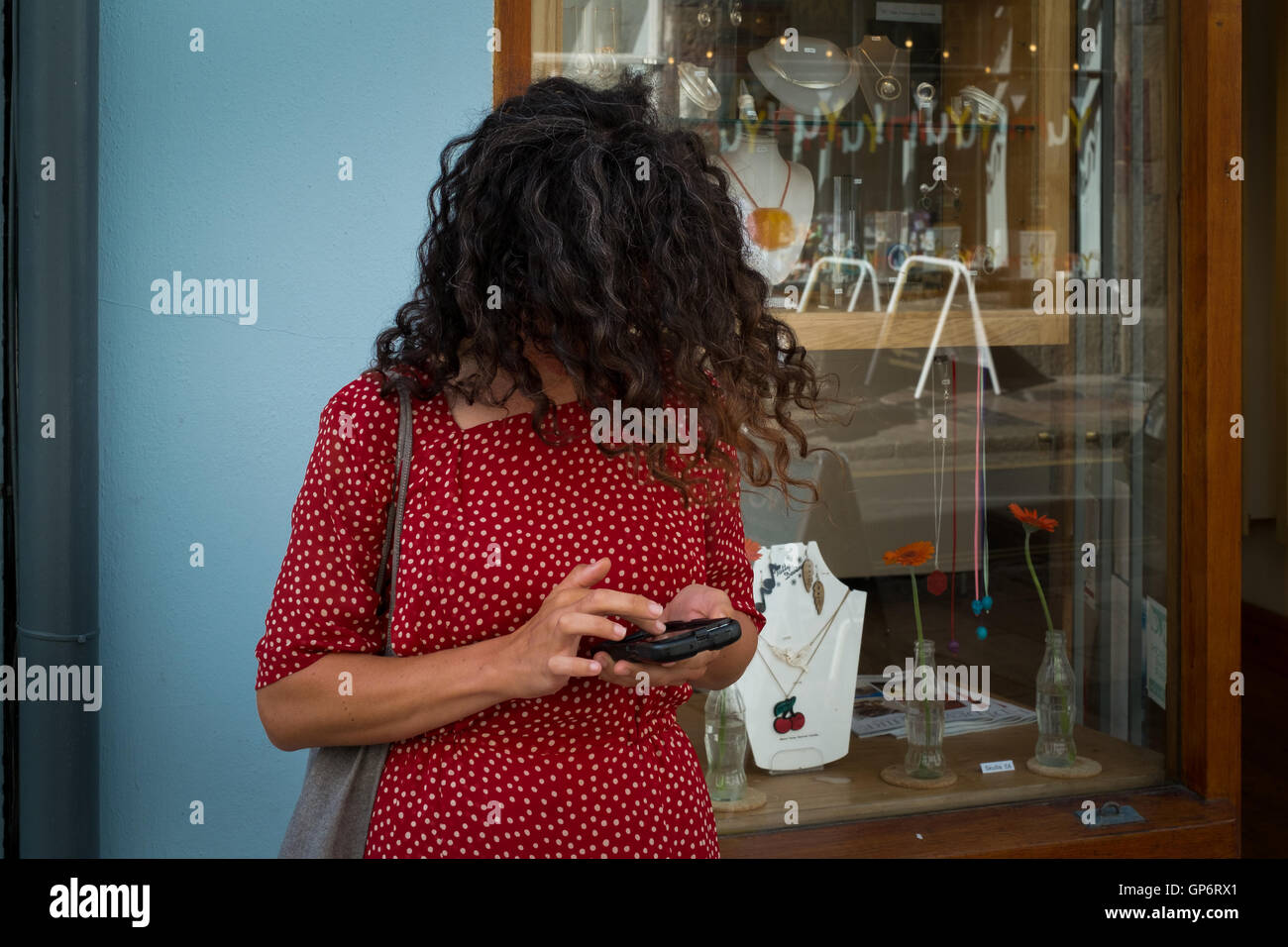 Eine Frau in einem roten Kleid, mit ihrem Gesicht fallenden Haare, beschäftigt sich auf ihrem Mobile Smartphone - Plymouth, 1. September 2016 Stockfoto