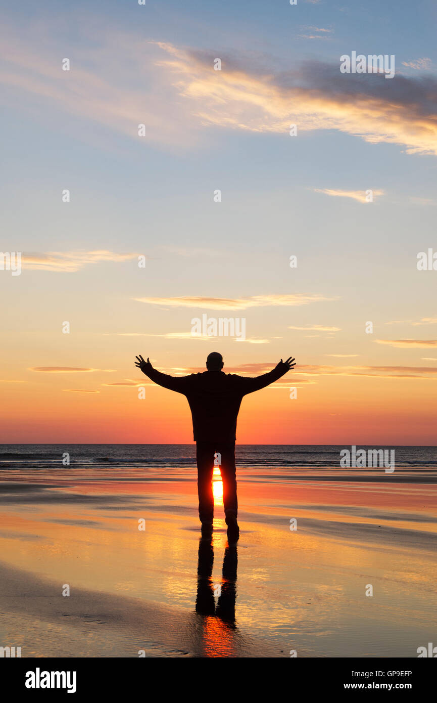 Silhouette Mann mit Armen angehoben bei Sonnenaufgang am Strand. Northumberland, England Stockfoto