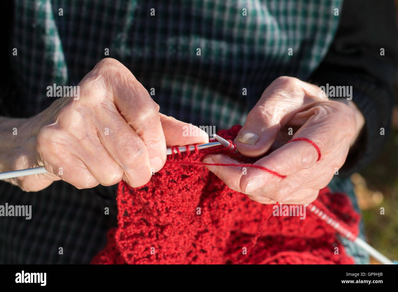 Ältere Frau Hände stricken mit roter Wolle im freien Stockfoto