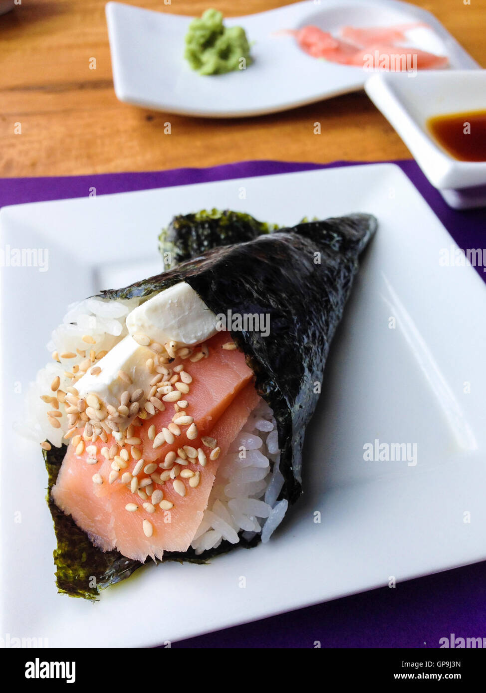 Sushirolle Hand gefüllt mit rohen Lachs, Reis, Frischkäse und Sesam vor Ingwer mit Wasabi und Sojasauce. Japanische Stockfoto
