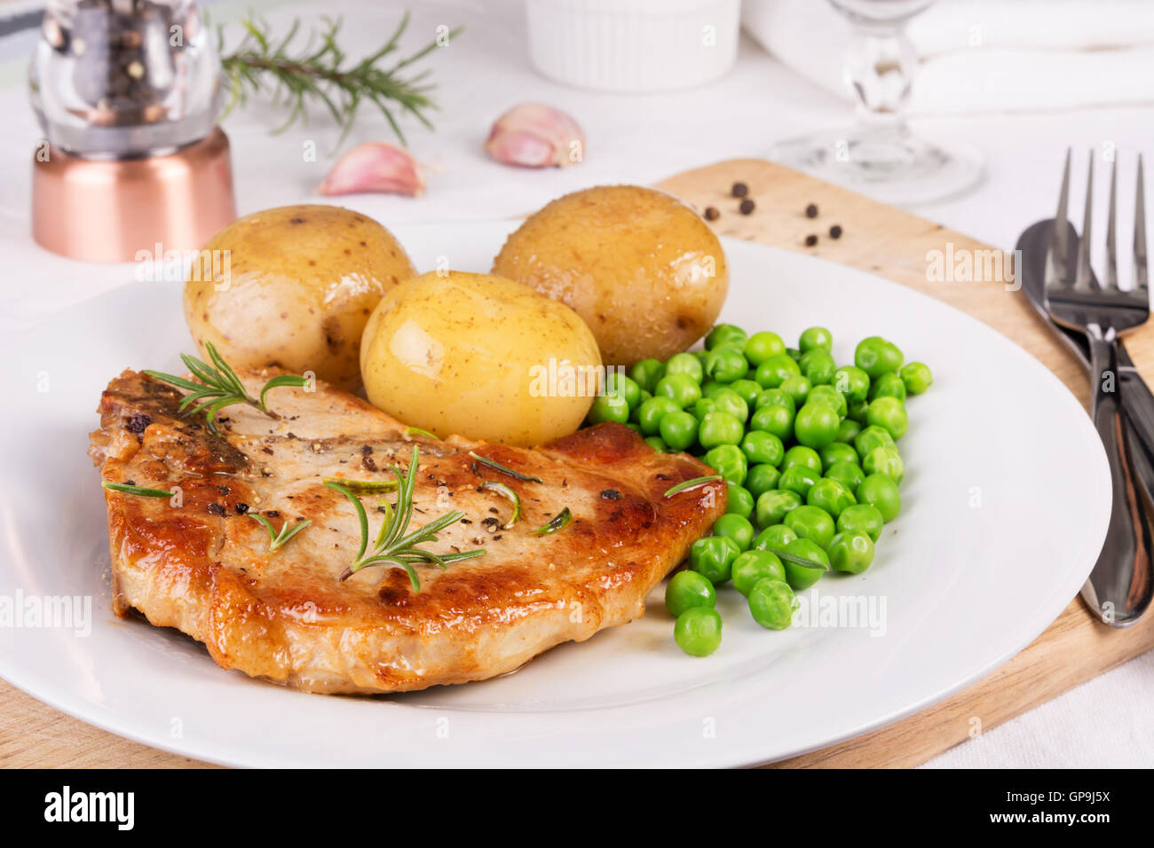 Schweinekotelett, gekochte Pellkartoffeln und grüne Erbsen auf dem Silbertablett serviert Stockfoto