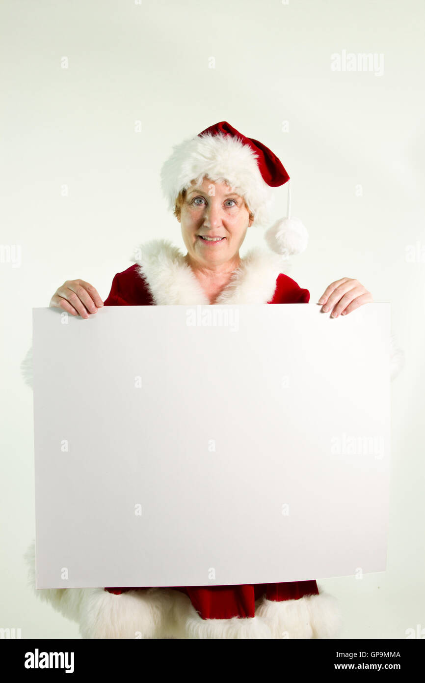 Reife Frau in Frau Claus oder Elfe Kostüm mit leeren schlicht weißen Schild. Stockfoto