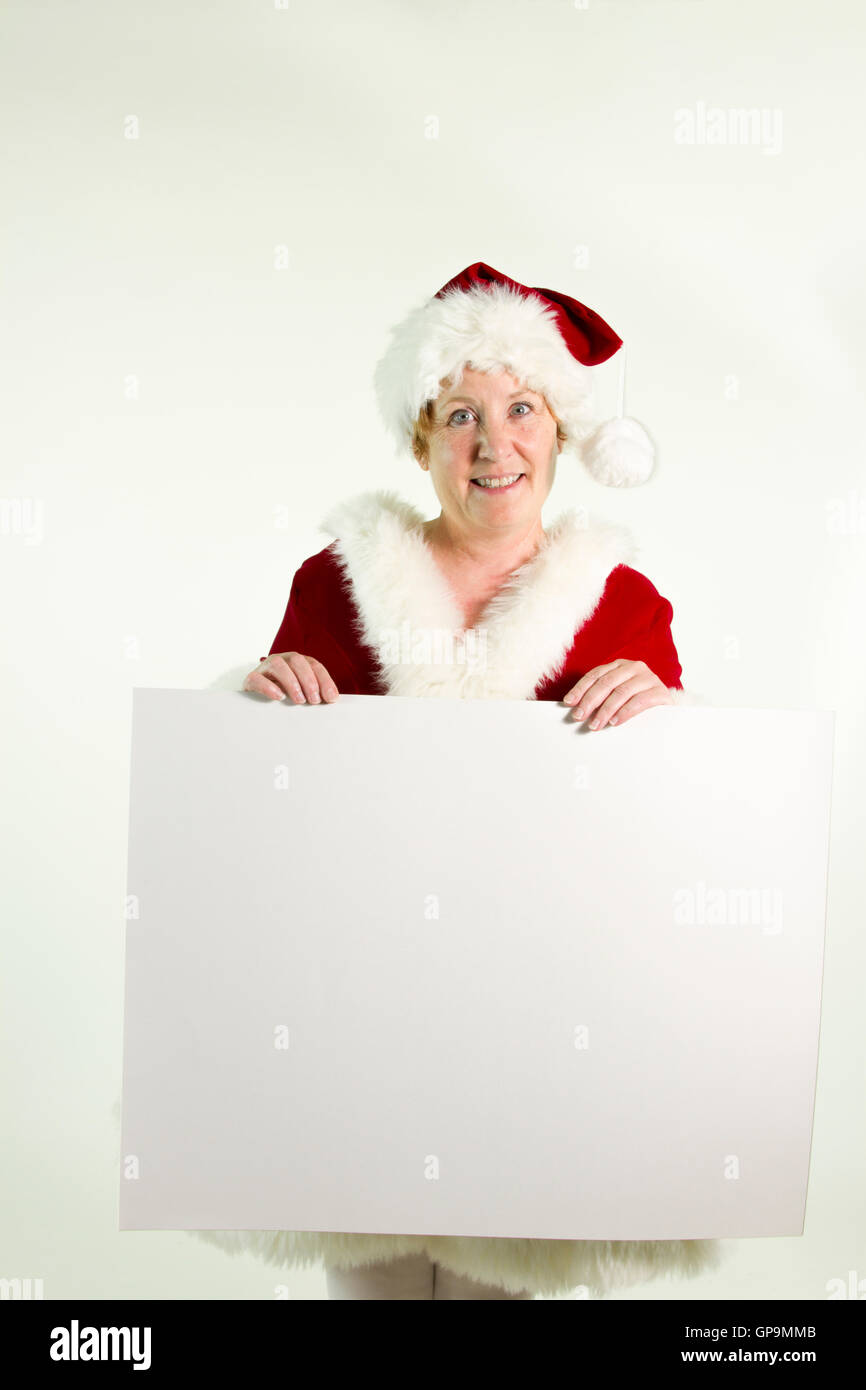 Reife Frau in Frau Claus oder Elfe Kostüm mit leeren schlicht weißen Schild. Stockfoto