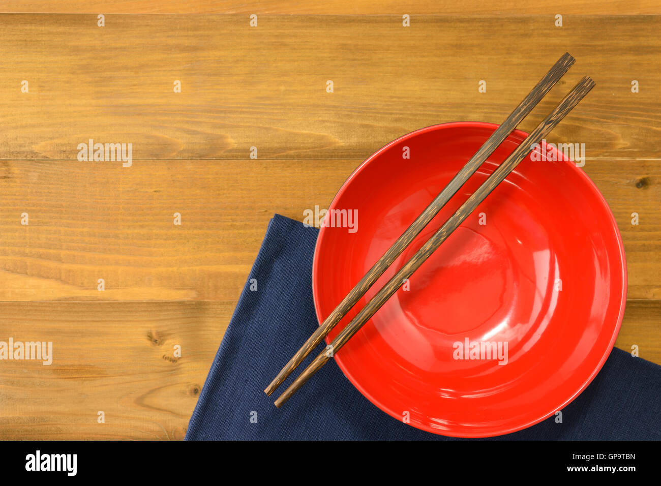 rote leere Schüssel mit Essstäbchen Holztisch und dunkle Blau napery Stockfoto
