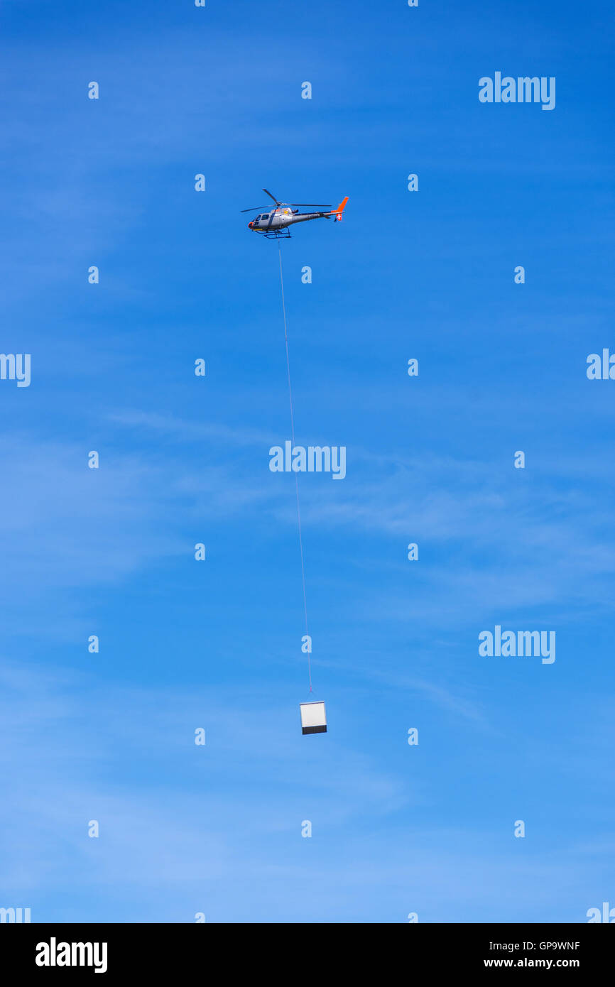 Hubschrauber gegen blauen Himmel, die Last auf das Ende des langen Kabels tragen Stockfoto