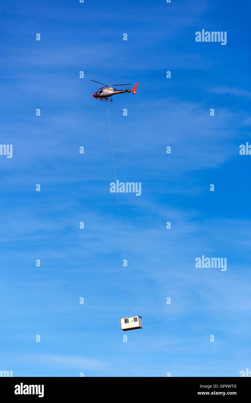 Hubschrauber gegen blauen Himmel, die Last auf das Ende des langen Kabels tragen Stockfoto
