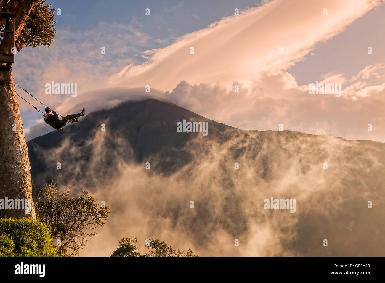 Silhouette der glücklicher junger Mann auf einer Schaukel mit Vulkan Tungurahua im Sonnenuntergang Hintergrund Stockfoto