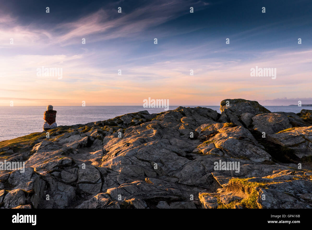 Eine Frau sitzt alleine auf dem Gipfel des Porth Insel in Newquay, Cornwall. Stockfoto
