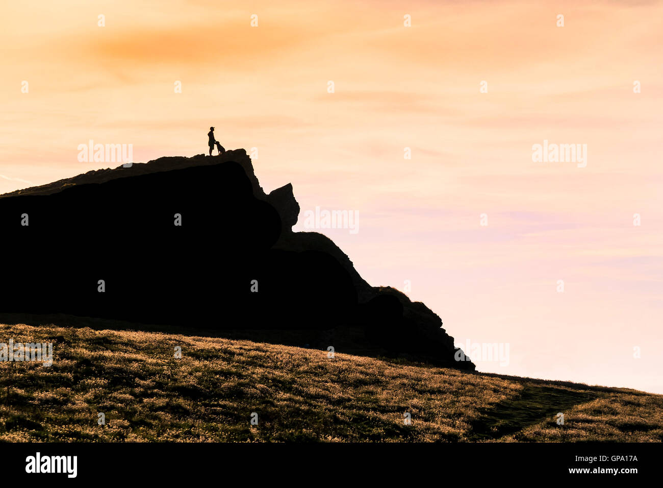 Die Silhouette eines Mannes und seinem Hund auf dem Gipfel des Trevelgue Head in Newquay, Cornwall. Stockfoto