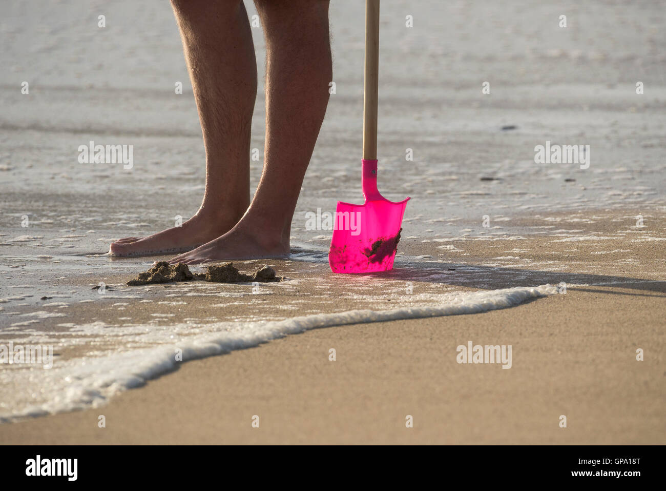 Die Beine von einem Urlauber stehen auf Fistral Beach und Hiolding eines Kindes Kunststoff Spaten. Newquay, Cornwall. Stockfoto