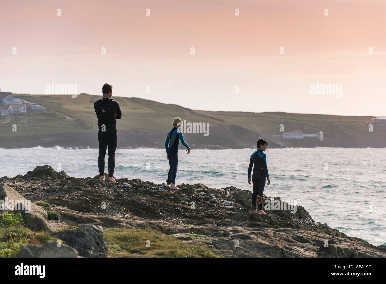 Ein Vater und seine zwei Söhne stehen auf Felsen über dem Meer auf den Towan Strand in Newquay, Cornwall. Stockfoto