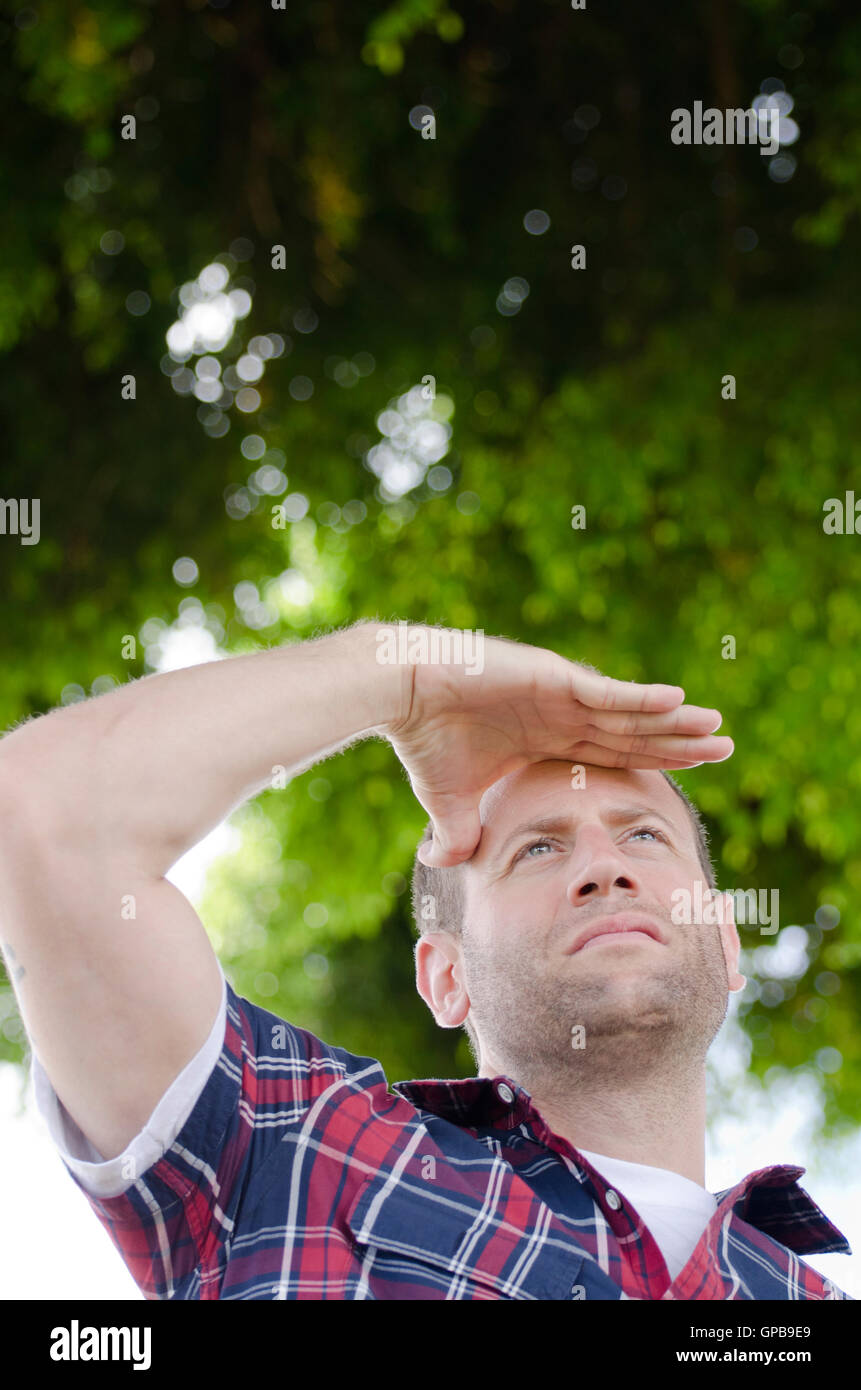 Verlässt der Mann Blick auf seine Zukunft mit seiner Hand über die Augen im Freien mit Grün im Hintergrund. Stockfoto
