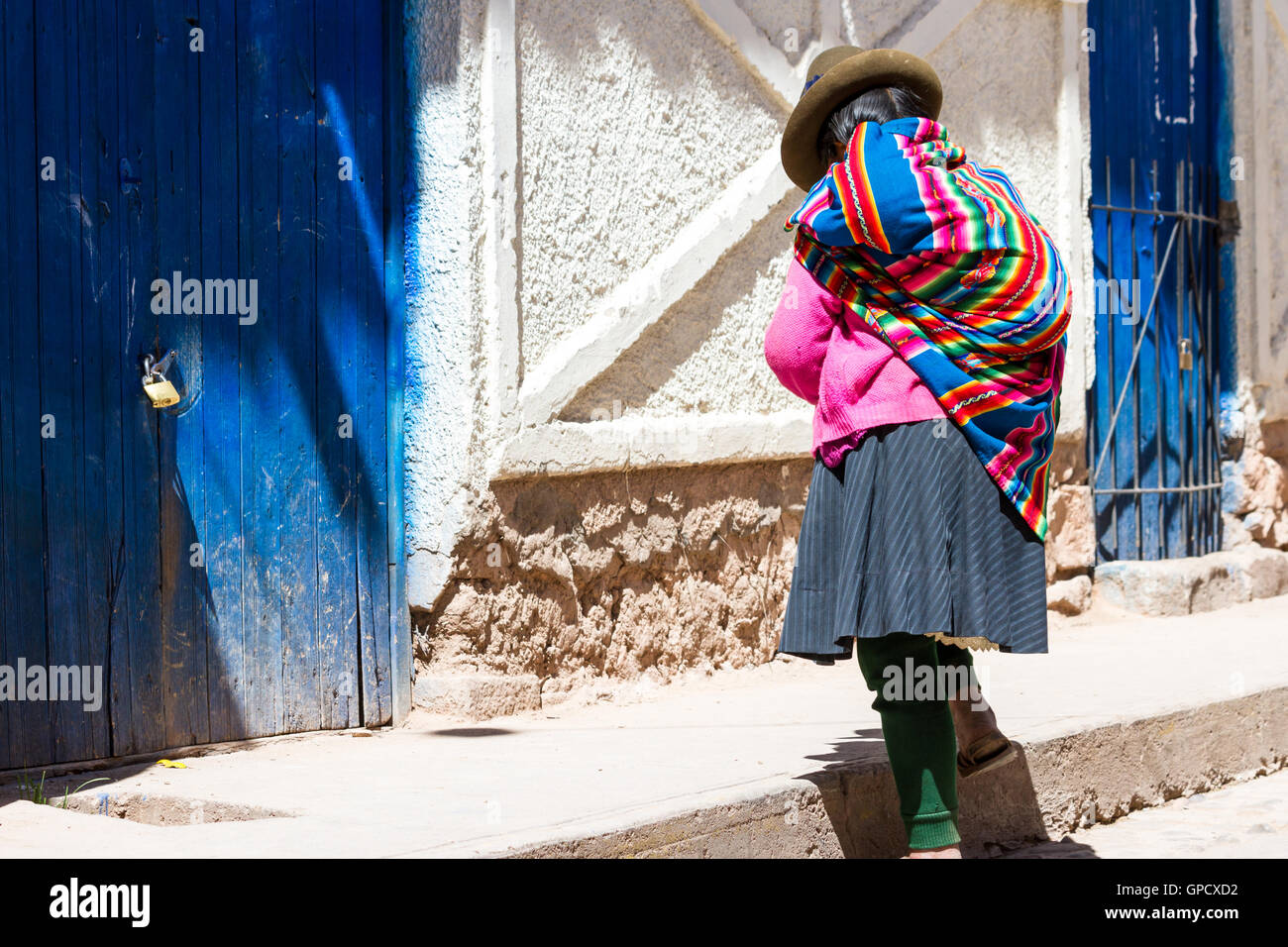 Maras Peru-Mai 18: einheimische Quechua-Frau mit schönen Farben, die zu Fuß in Richtung einer blauen Tür. 18. Mai 2016, Maras Peru. Stockfoto