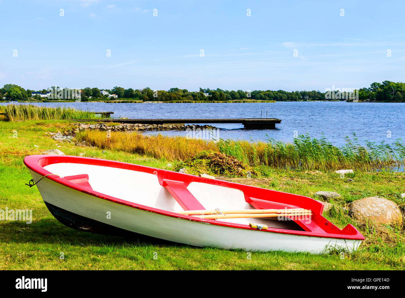 Kleine rotes und weißes Ruderboot gezogen auf dem Land mit der Küste im Hintergrund.  Skavkulla in Karlskrona Schären, Schwede Stockfoto
