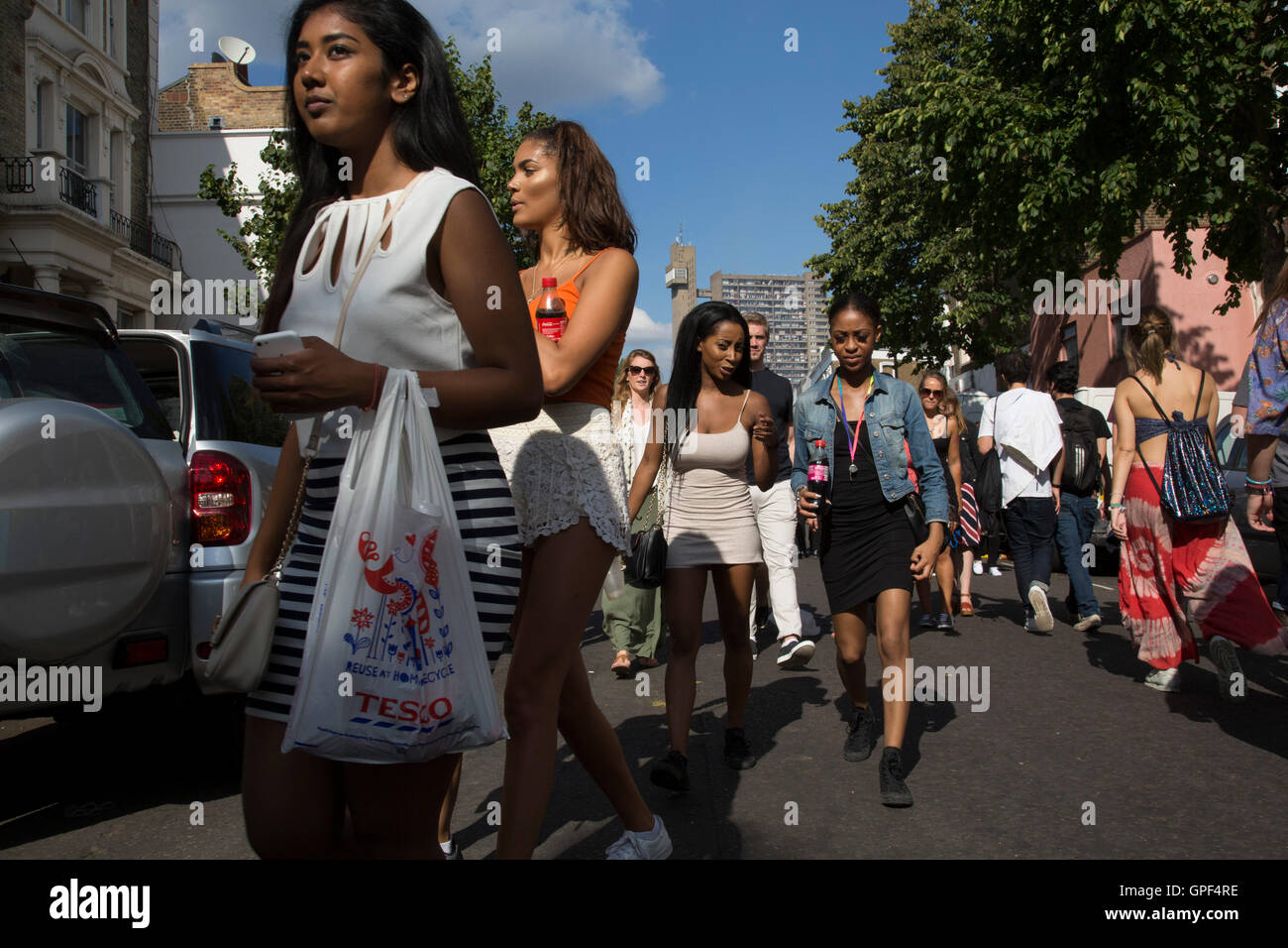 Gruppe von Freunden zu Fuß entlang Golborne Road mit Trellick Tower in der Ferne auf Sonntag, 28. August 2016 bei den 50. Notting Hill Carnival in Westlondon. Ein Fest der Westindischen / Karibik Kultur und Europas größte Straßenparty, Festival und Parade. Nachtschwärmer kommen in hunderttausenden zum Spaß haben, tanzen, trinken und loslassen in die tolle Atmosphäre. Es wird geführt von den Mitgliedern der West-indischen / Karibische Gemeinschaft, besonders die Trinidad und Tobagonian britische Bevölkerung, von denen viele seit den 1950er Jahren in der Gegend gelebt haben. Der Karneval hat bis zu 2 Millionen Menschen angezogen. Stockfoto