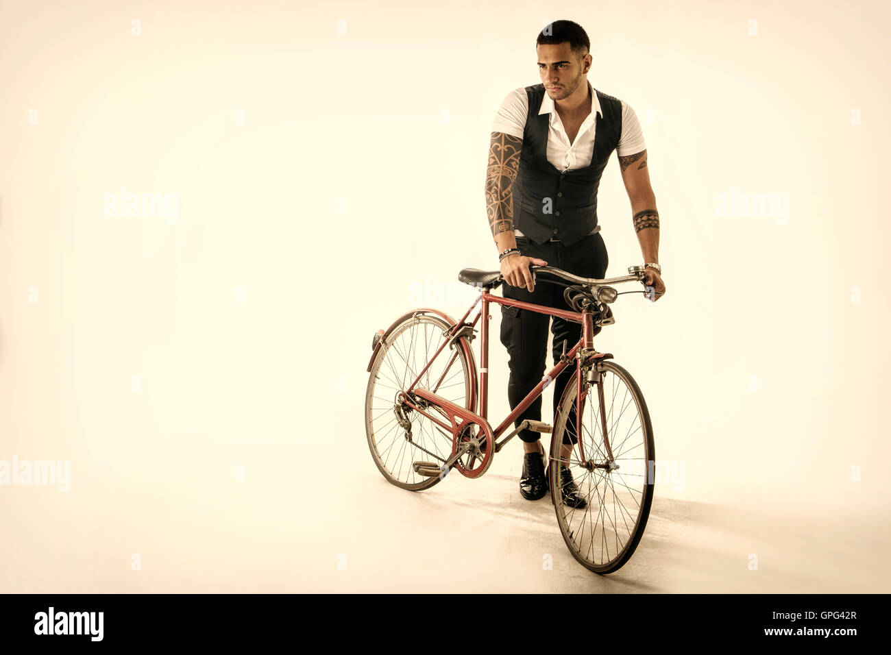 Porträt des jungen tätowierte Mann in eleganten Kleidern und Schuhen mit dem Fahrrad. Studio gedreht. Ganzkörperfoto Stockfoto