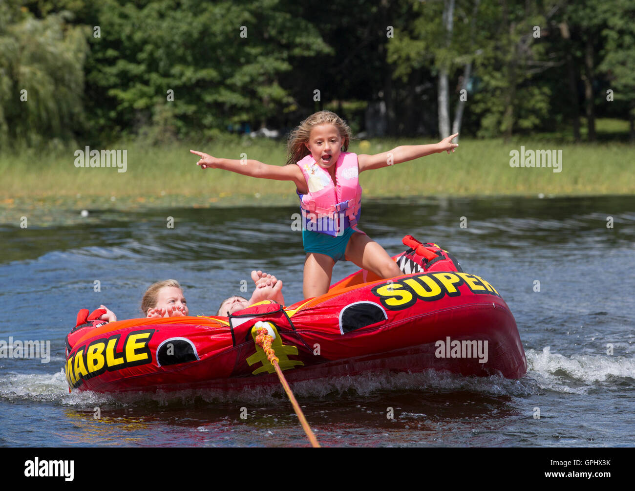 Ein junges Mädchen steht auf einem aufblasbaren Fahrt gezogen hinter einem Schnellboot auf Little Pine Lake in Minnesota Stockfoto