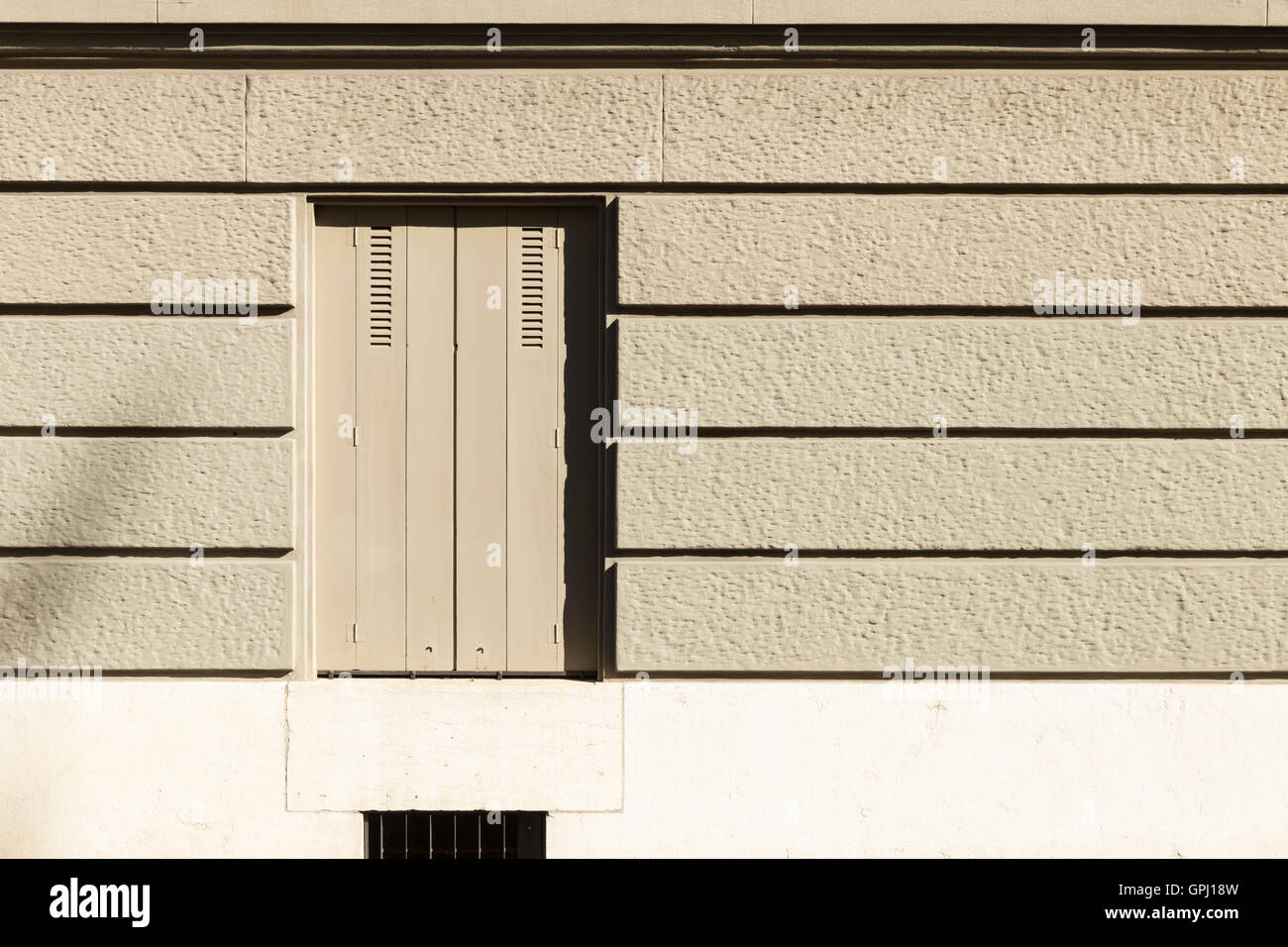 Eine graue bemalte Wand mit Querstreifen und einem Fenster mit geschlossenen Fensterläden. Stockfoto