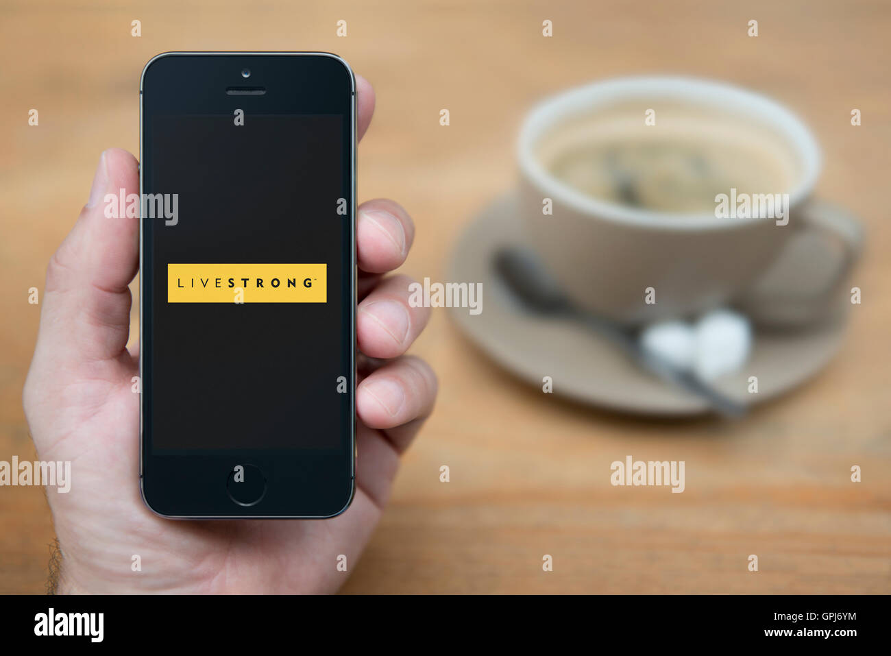 Ein Mann schaut auf seinem iPhone die Live Strong-Logo anzeigt, während bei einer Tasse Kaffee (nur zur redaktionellen Verwendung) saß. Stockfoto