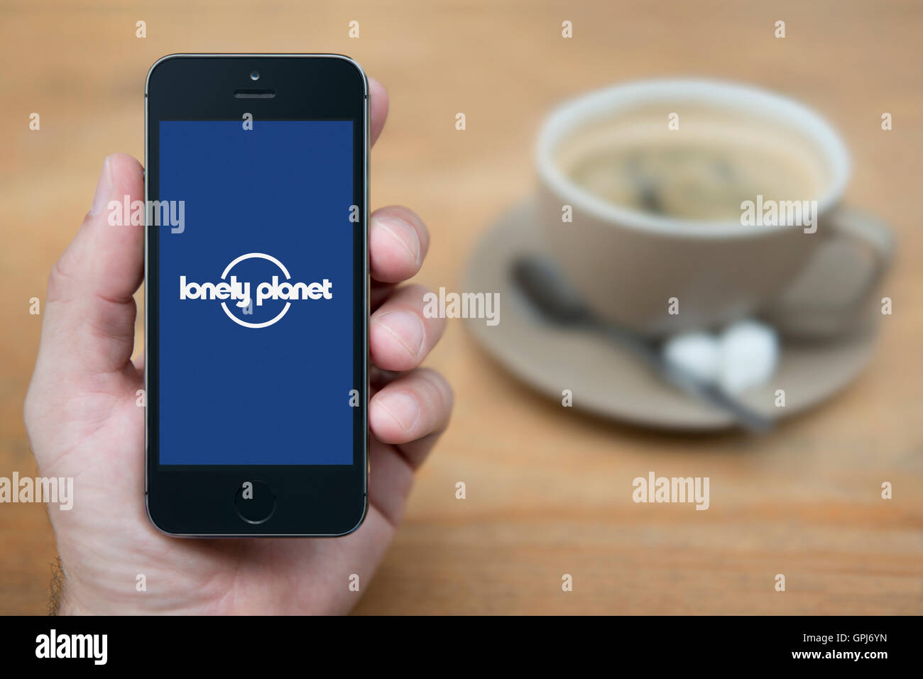 Ein Mann schaut auf seinem iPhone die Lonely Planet-Logo anzeigt, während bei einer Tasse Kaffee (nur zur redaktionellen Verwendung) saß. Stockfoto
