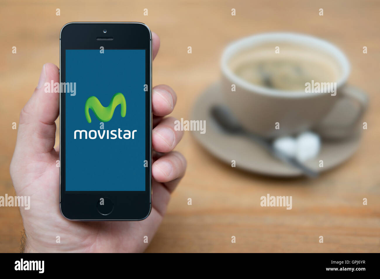 Ein Mann schaut auf seinem iPhone das das Betreiberlogo Movistar Telekommunikation mit Kaffee (nur zur redaktionellen Verwendung) anzeigt. Stockfoto