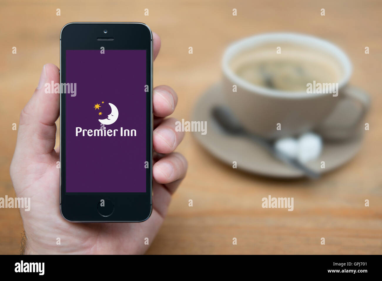Ein Mann schaut auf seinem iPhone die das Premier Inn-Logo anzeigt, während bei einer Tasse Kaffee (nur zur redaktionellen Verwendung) saß. Stockfoto