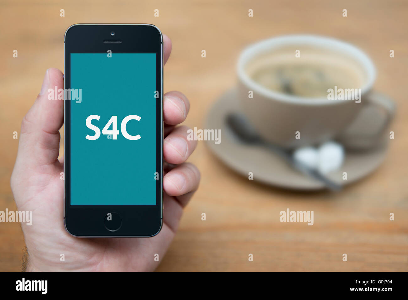 Ein Mann schaut auf seinem iPhone das das Senderlogo S4C Wales Fernsehen mit Kaffee (nur zur redaktionellen Verwendung) anzeigt. Stockfoto