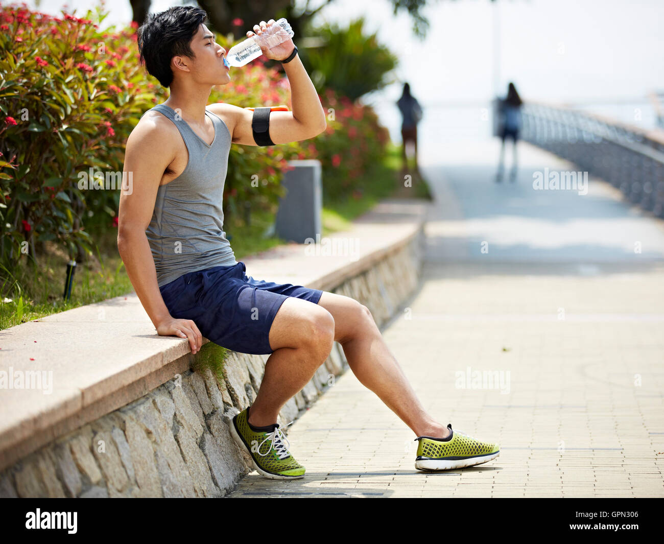 junge hübsche asiatische Jogger nehmen eine Pause und Trinken von Wasser aus einer Flasche, Seitenansicht Stockfoto