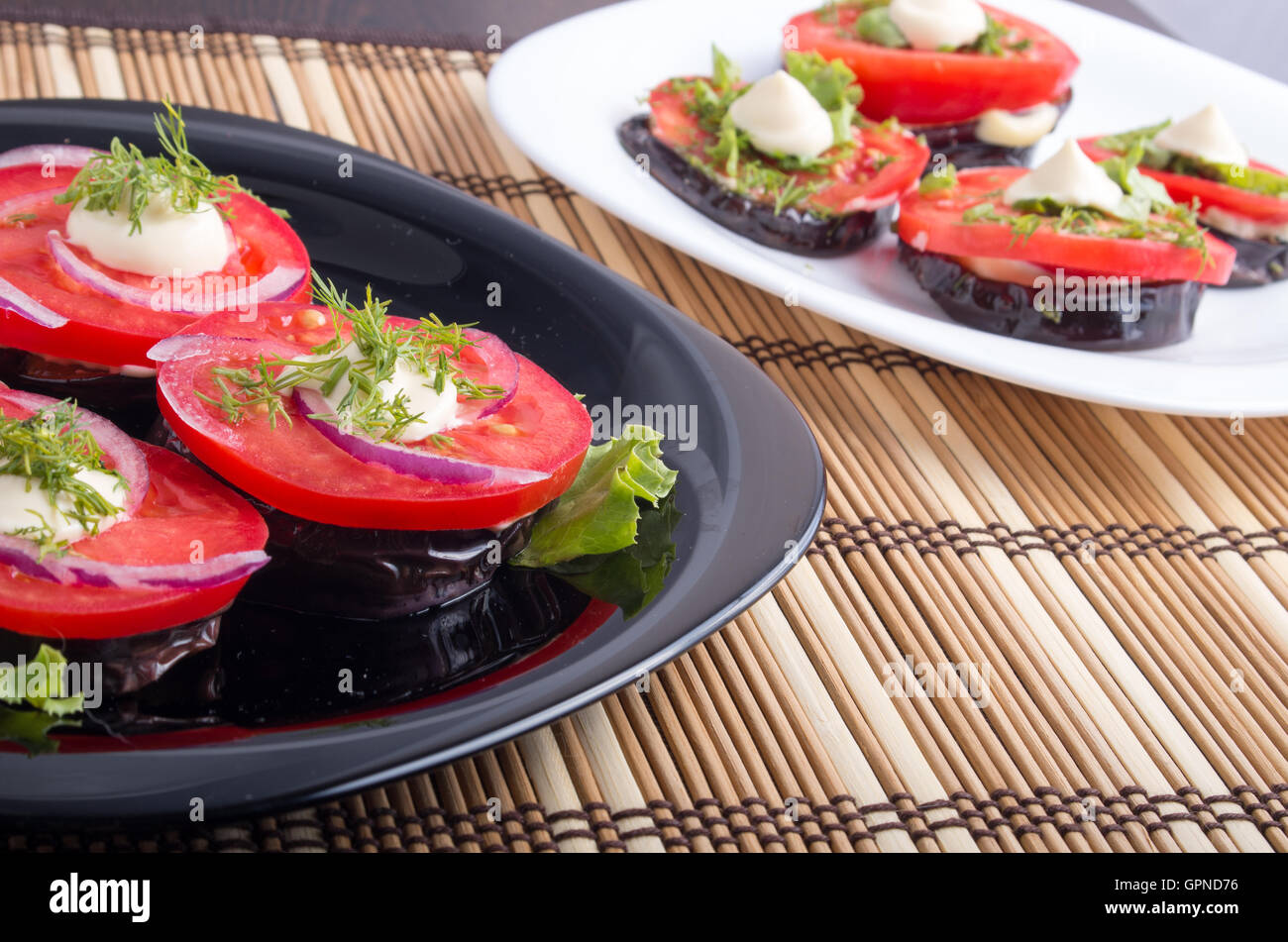 Gemüsegerichte geschmorte Auberginen und frische rote Tomate Nahaufnahme mit geringer Tiefe des Fokus auf die braune Bambusmatte Stockfoto