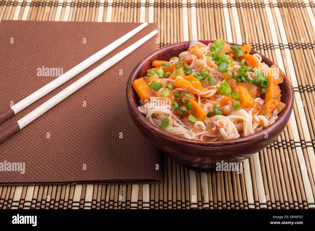 Eine Portion Reis Vermicelli Hu-Teu mit Gemüse Karotte Sauce in einer kleinen braunen Holzschale auf einer gestreiften Matte in der Nähe der hölzernen Stockfoto