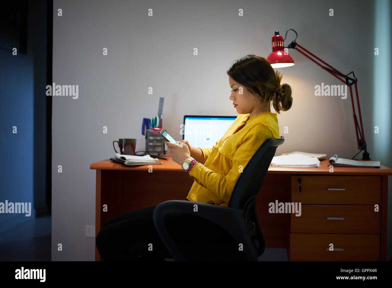Junge Frau mit Smartphone während der Hausaufgaben in der Nacht. Weibliche College-Student studiert und SMS mit Handy Stockfoto