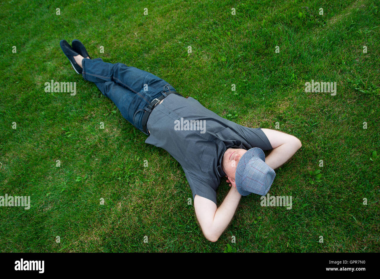 Mann liegt in einem Feld auf dem grünen Rasen mit dem Hut übers Gesicht Stockfoto