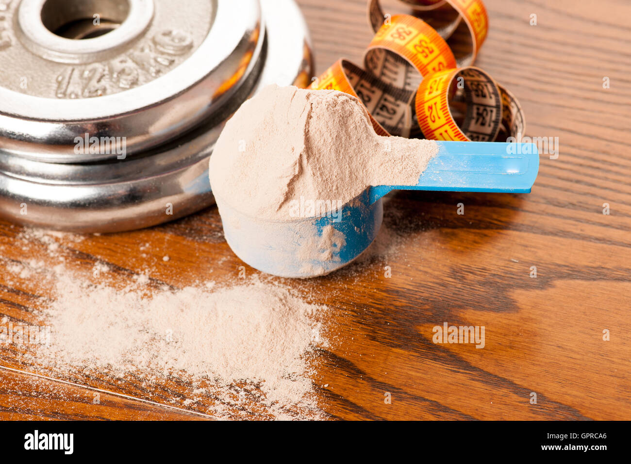 Molke-Protein-Pulver in Mess-Schaufel, m-Band und Hantel auf hölzernen Hintergrund. Stockfoto