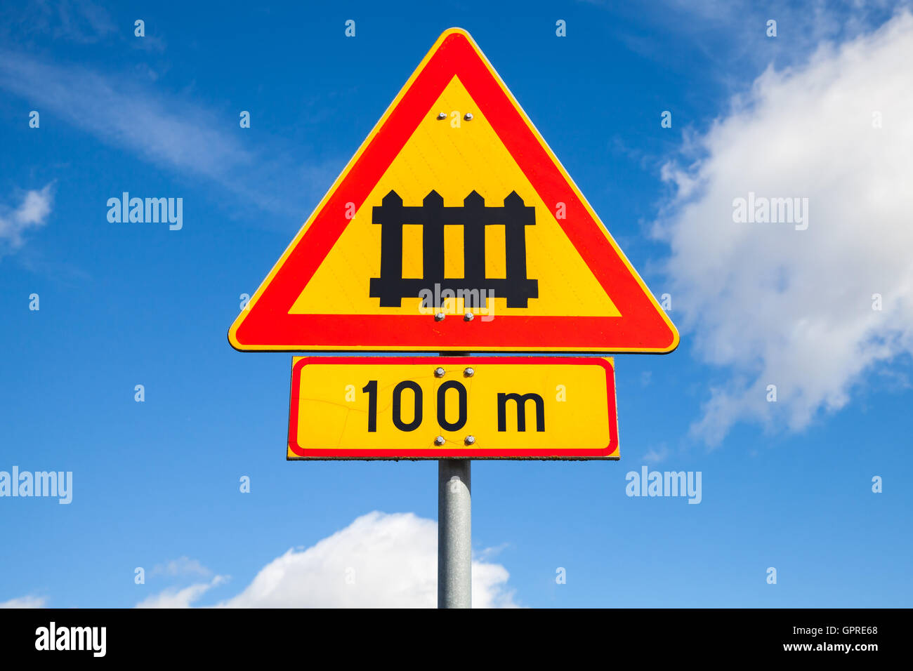 Schweden-Bahnübergang mit Tor Zeichen. Dreieckige Warnung Roadsign mit roten Rand und 100m Entfernung-Etikett über blauen Wolkenhimmel Stockfoto