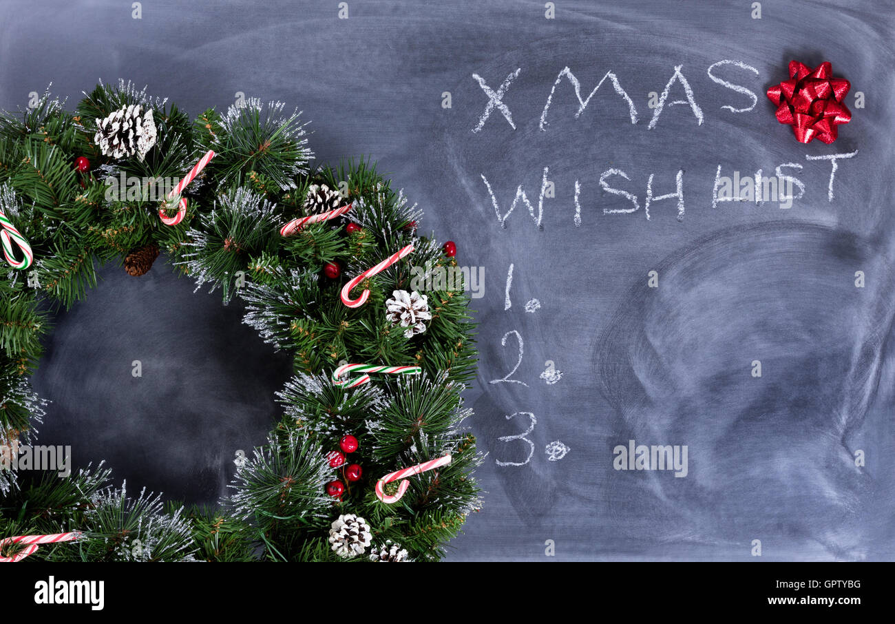 Kranz, Geschenk Bogen und Candy Canes auf gelöschte Tafel mit Weihnachts-Wunschliste geschrieben an Bord. Stockfoto