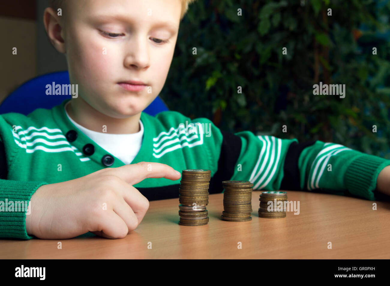 Glückliches Kind (junge, Kind, Teenager) Stapel von Münzen auf dem Tisch machen. Kinder und Geld Konzept. Stockfoto