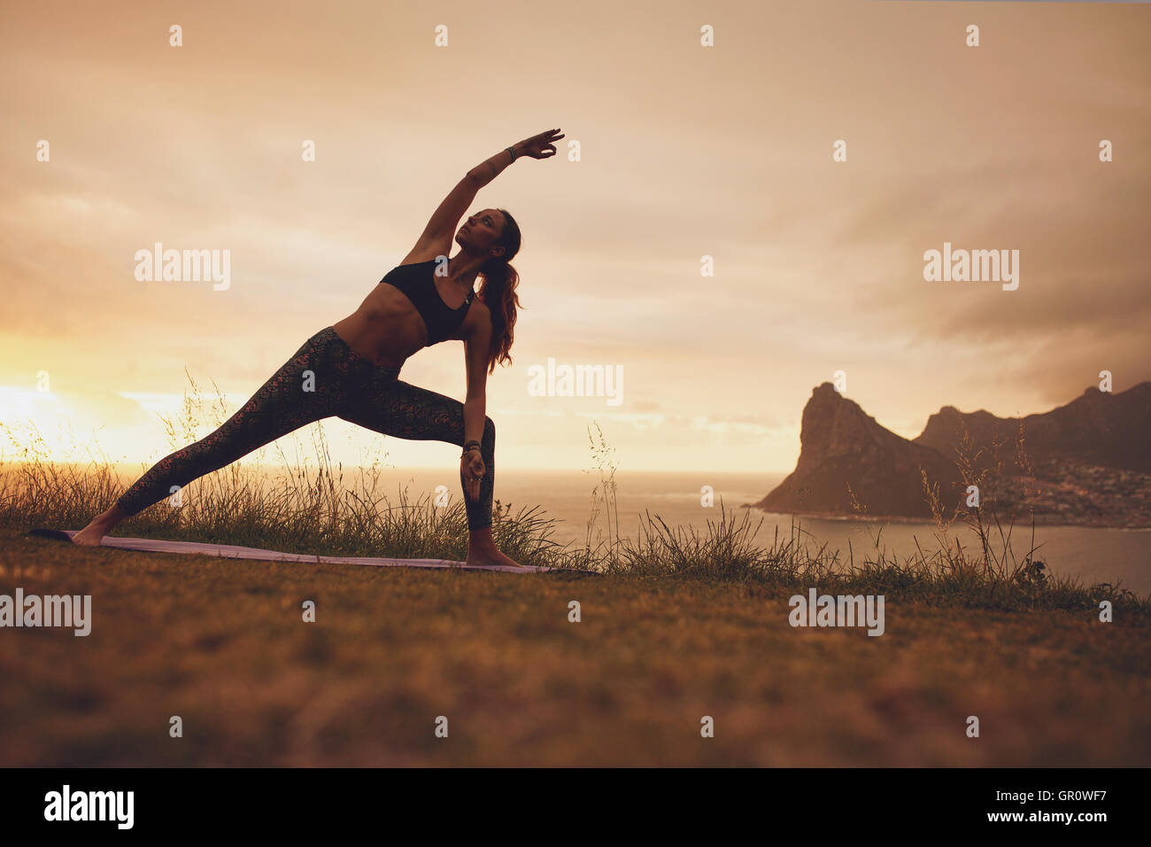 Voller Länge Schuss jungen Frau Utthita Parsvakonasana Yoga Asana üben. Gesunde Frauen trainieren bei Sonnenuntergang auf der Klippe. Stockfoto