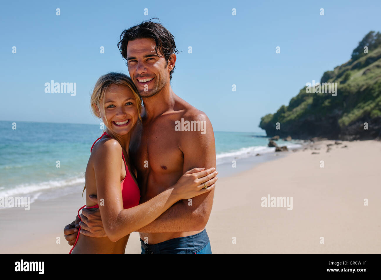 Porträt der fröhliche junge Paar zusammen am Strand stehen. Mann und Frau am Ufer Meeres Blick in die Kamera und lächelnd. Stockfoto
