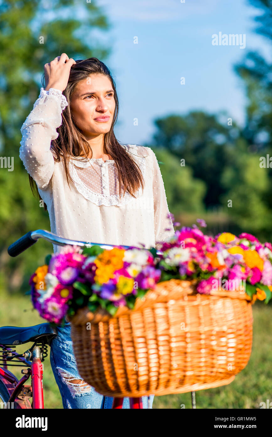 Junge Mädchen posiert mit einem Fahrrad mit einem Korb voller Blumen Stockfoto