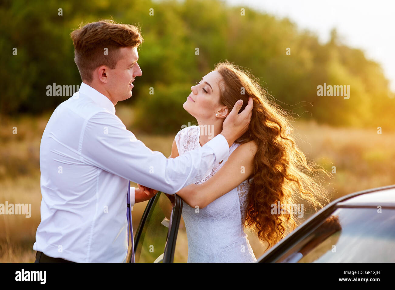 Glückliche Braut und Bräutigam umarmen in der Nähe von Auto Stockfoto
