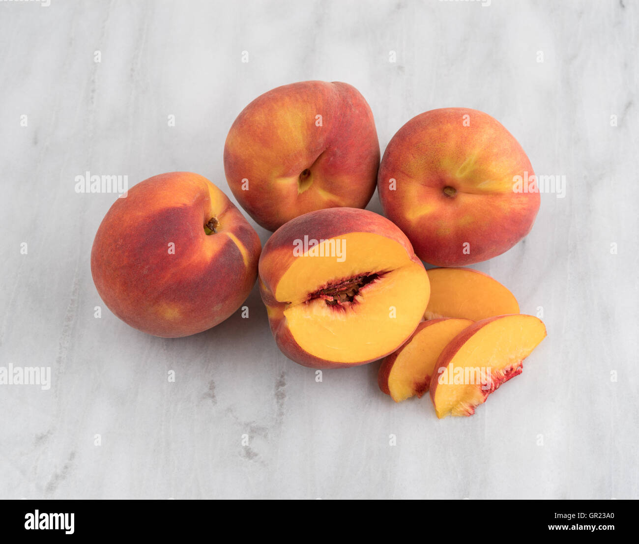 Eine Gruppe von ganzen Nektarinen mit einer Scheibe aus einer Frucht auf ein grauer Marmor Schneidebrett entfernt. Stockfoto