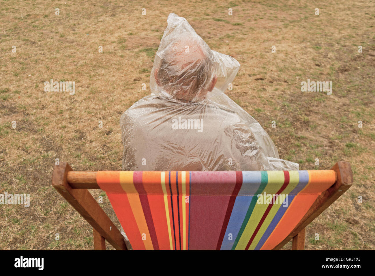 Ein älterer Mann im Liegestuhl, tragen einen Kunststoff Regenponcho. Stockfoto
