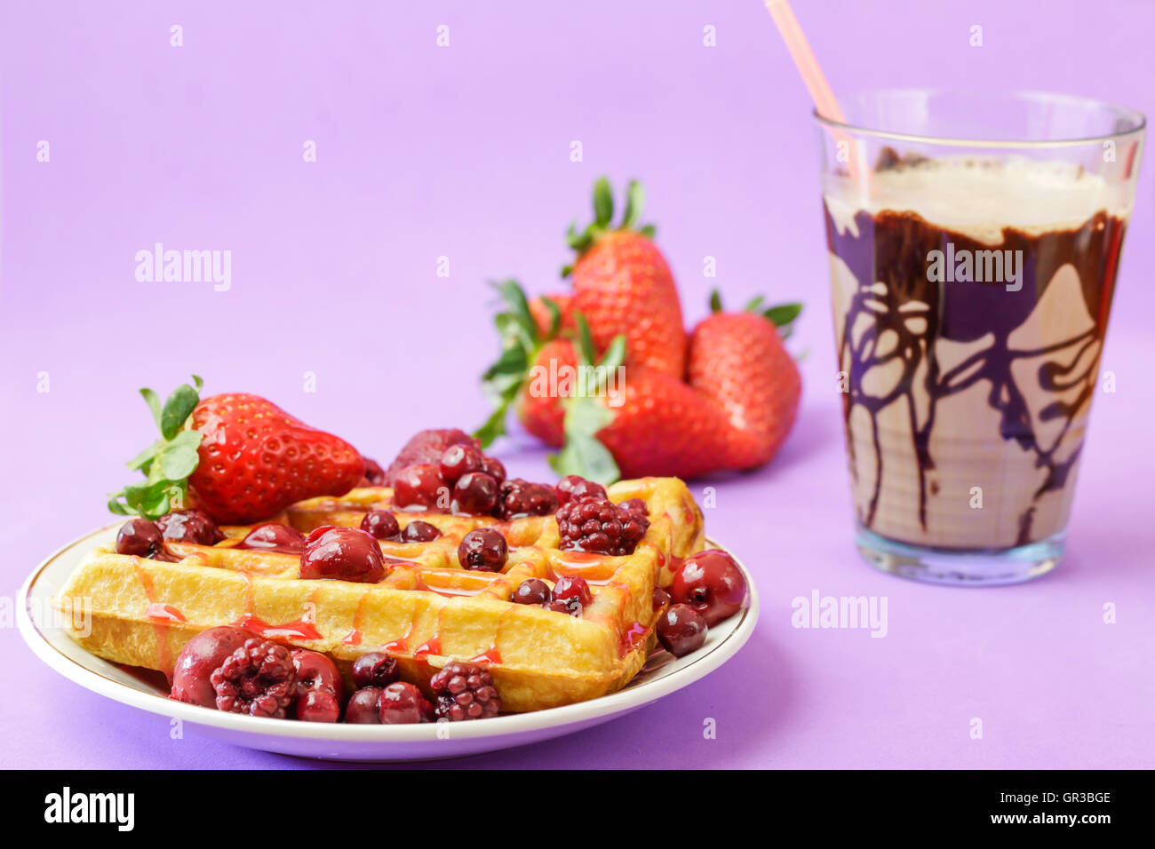 Nahaufnahme von leckeren Waffeln mit roten Beeren und Schokolade Smoothy auf violettem Hintergrund Stockfoto