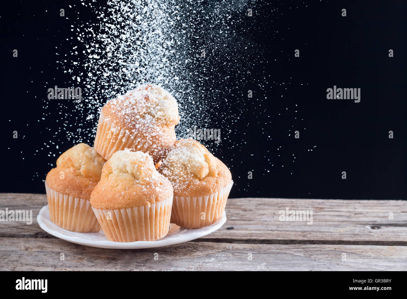 Gießen Zucker auf frische hausgemachte Muffins mit schwarzem Hintergrund Stockfoto