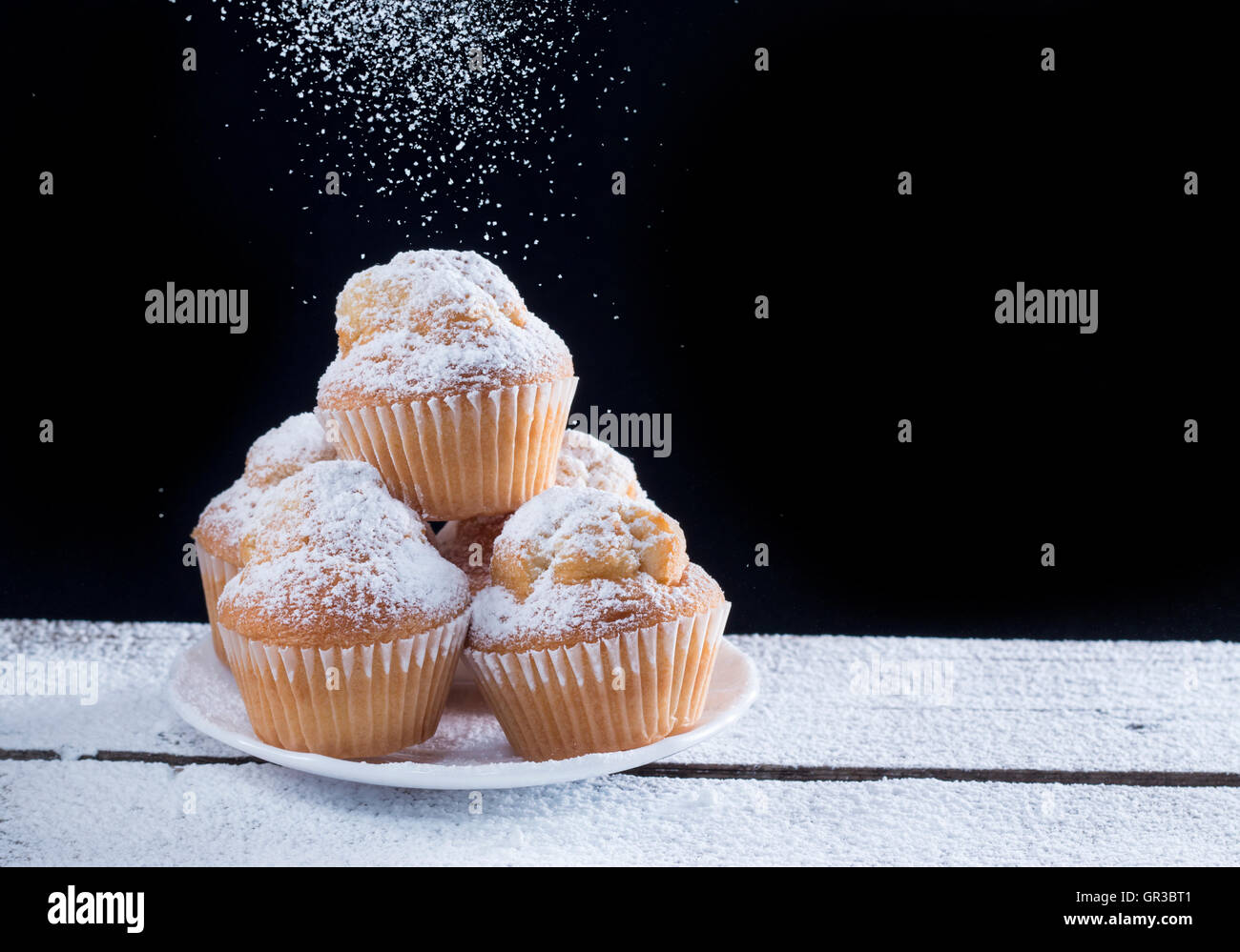 Gießen Zucker auf frische hausgemachte Muffins mit schwarzem Hintergrund Stockfoto
