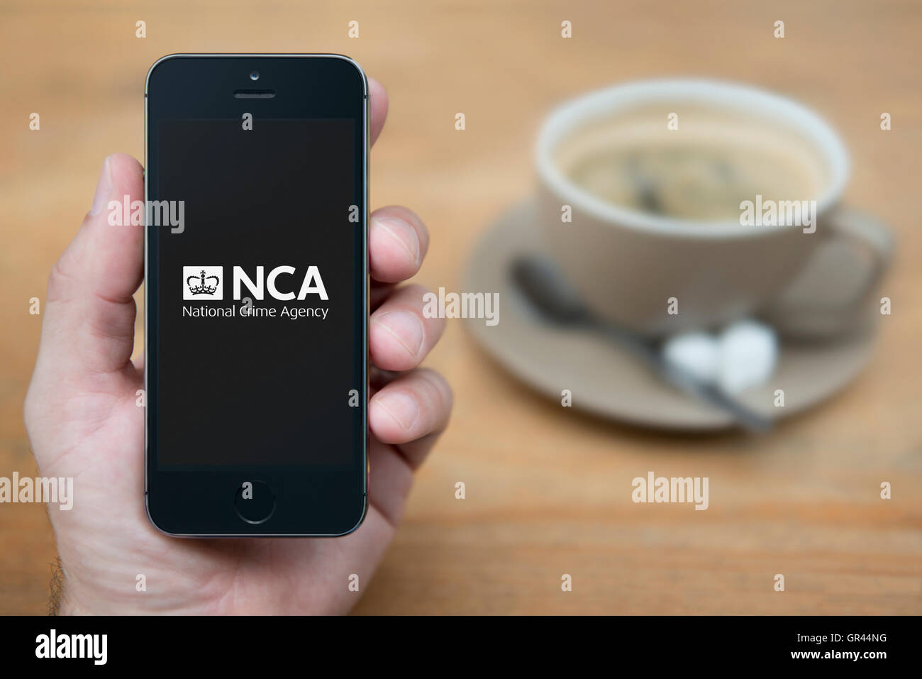 Ein Mann schaut auf seinem iPhone die UK Regierung National Crime Agency NCA-Logo (nur zur redaktionellen Verwendung) anzeigt. Stockfoto