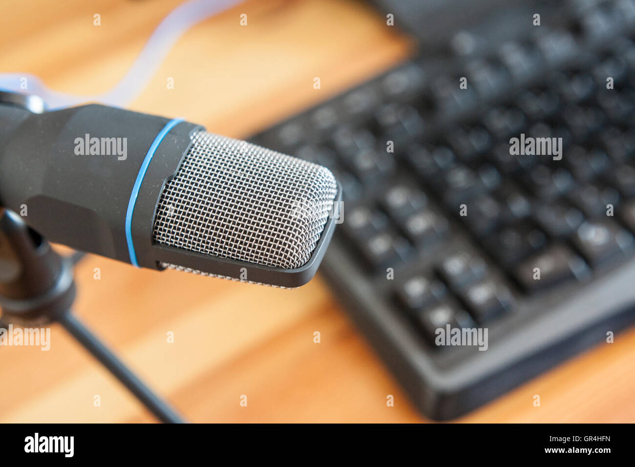 Professionelles Mikrofon mit Computer-Tastatur über hölzerne Desktop-Oberfläche. Podcast-Konzept Stockfoto